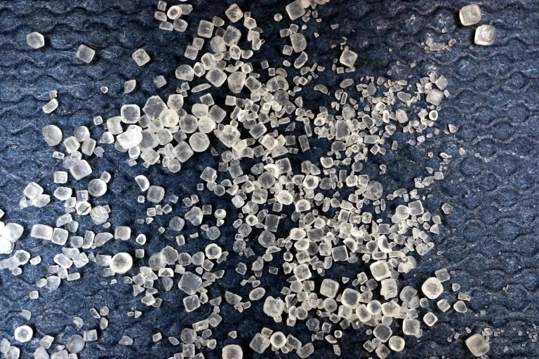 White and clear cubic salt crystals scattered on a dark surface